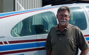 bearded man stands next to a Beechcraft Bonanza